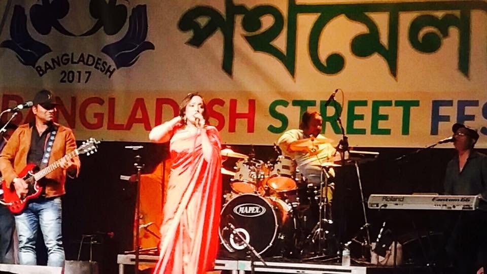 Rowshanara Moni singing on an outdoor festival stage with a full band — guitarist, drummer and keyboard player