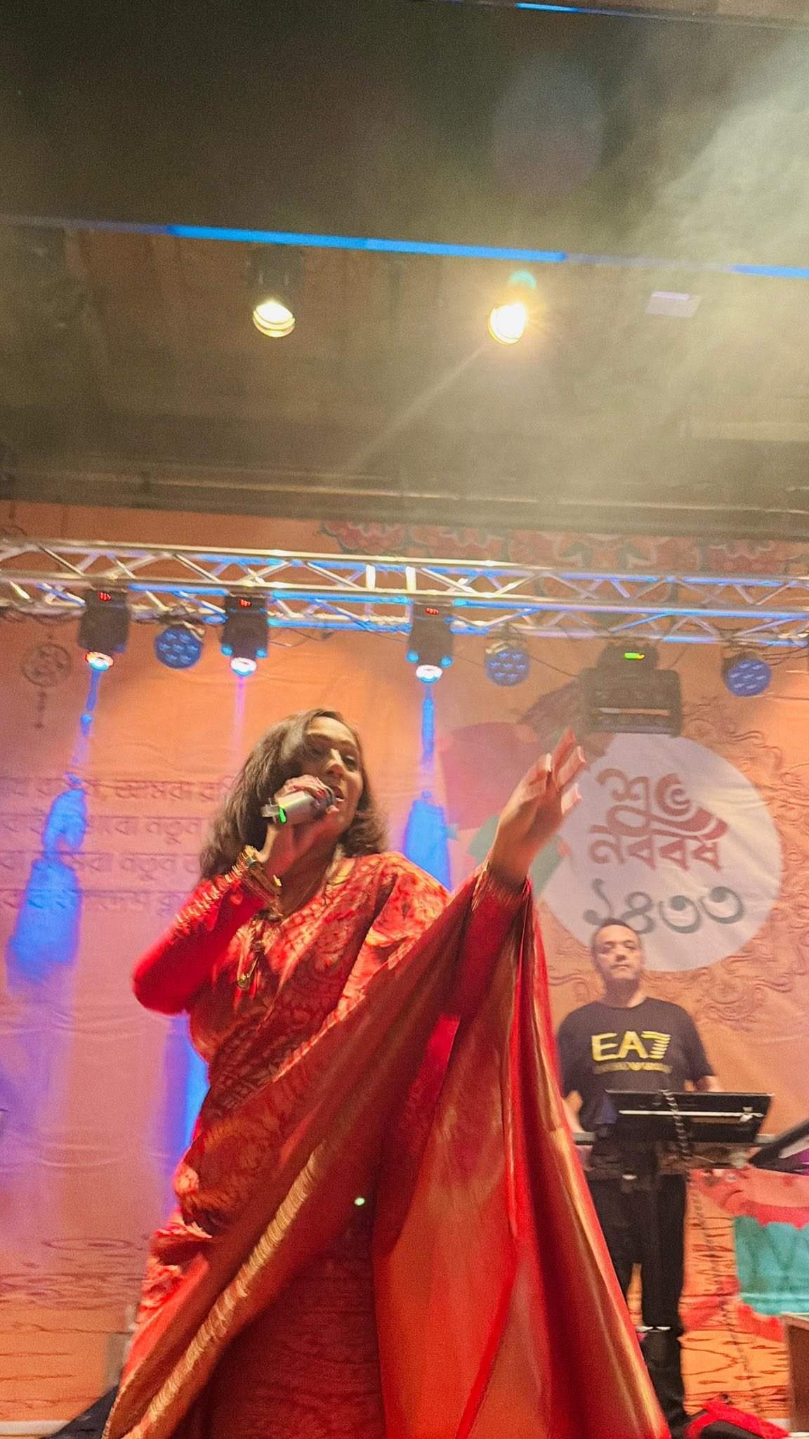 Rowshanara Moni performing in a red sari with one arm outstretched under stage lighting