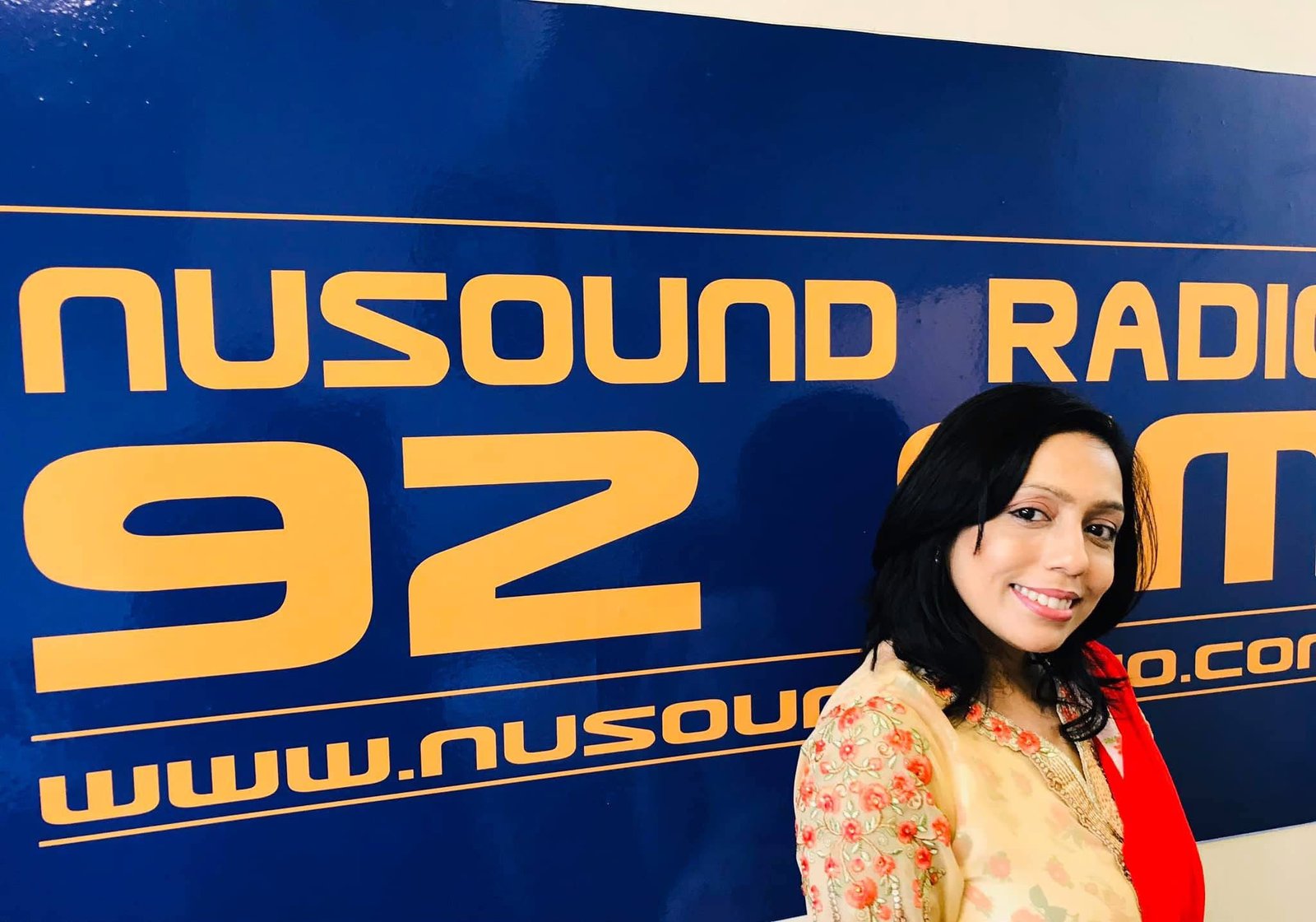Rowshanara Moni beside a Nusound Radio 92 FM banner
